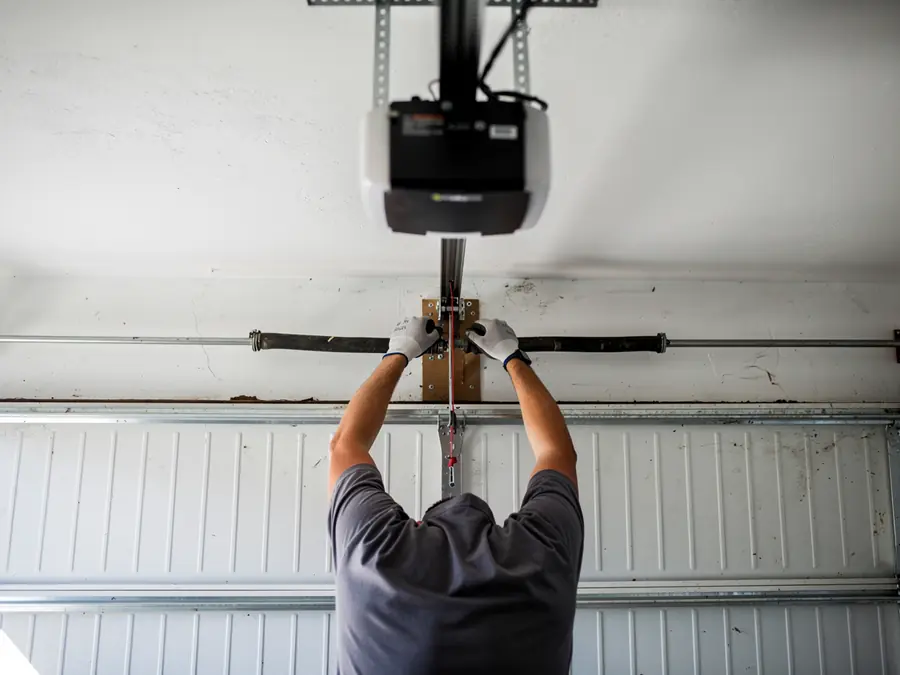 A technician adjusts a torsion spring above a white garage door.