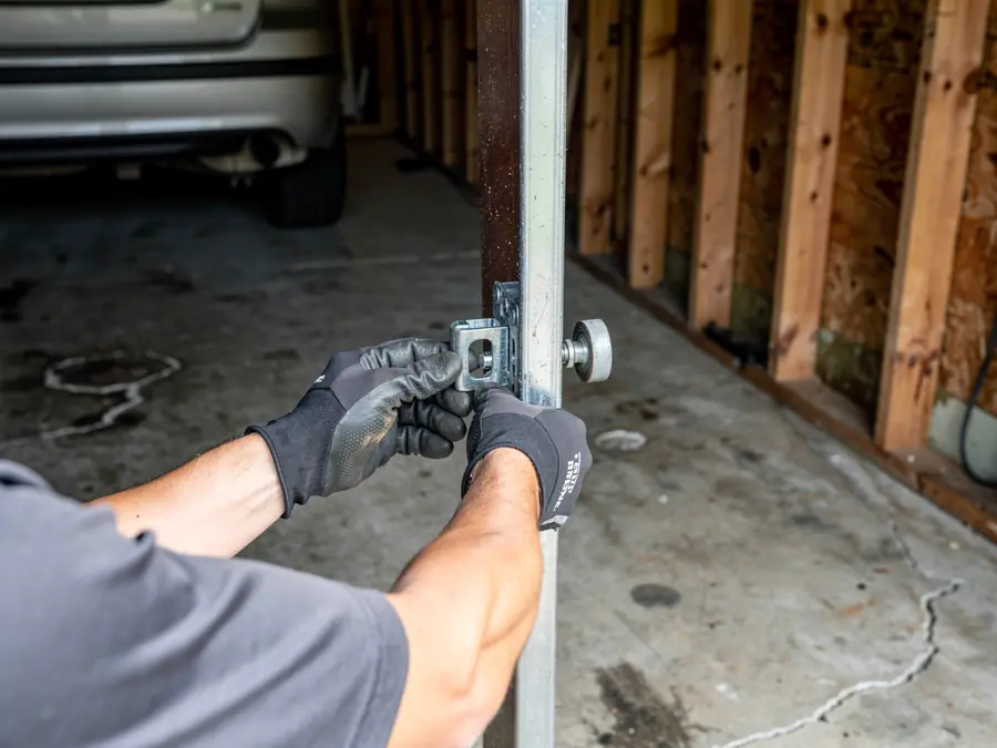 A technician in gloves adjusts a garage door roller on a track.