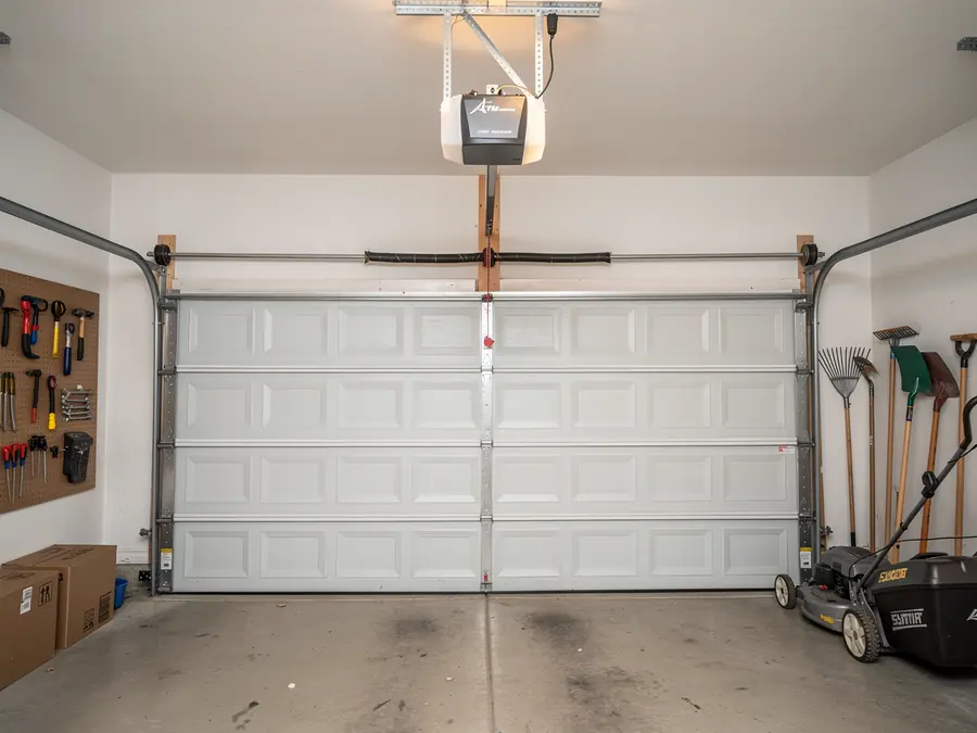 A white garage door is closed, with an opener and torsion spring visible.
